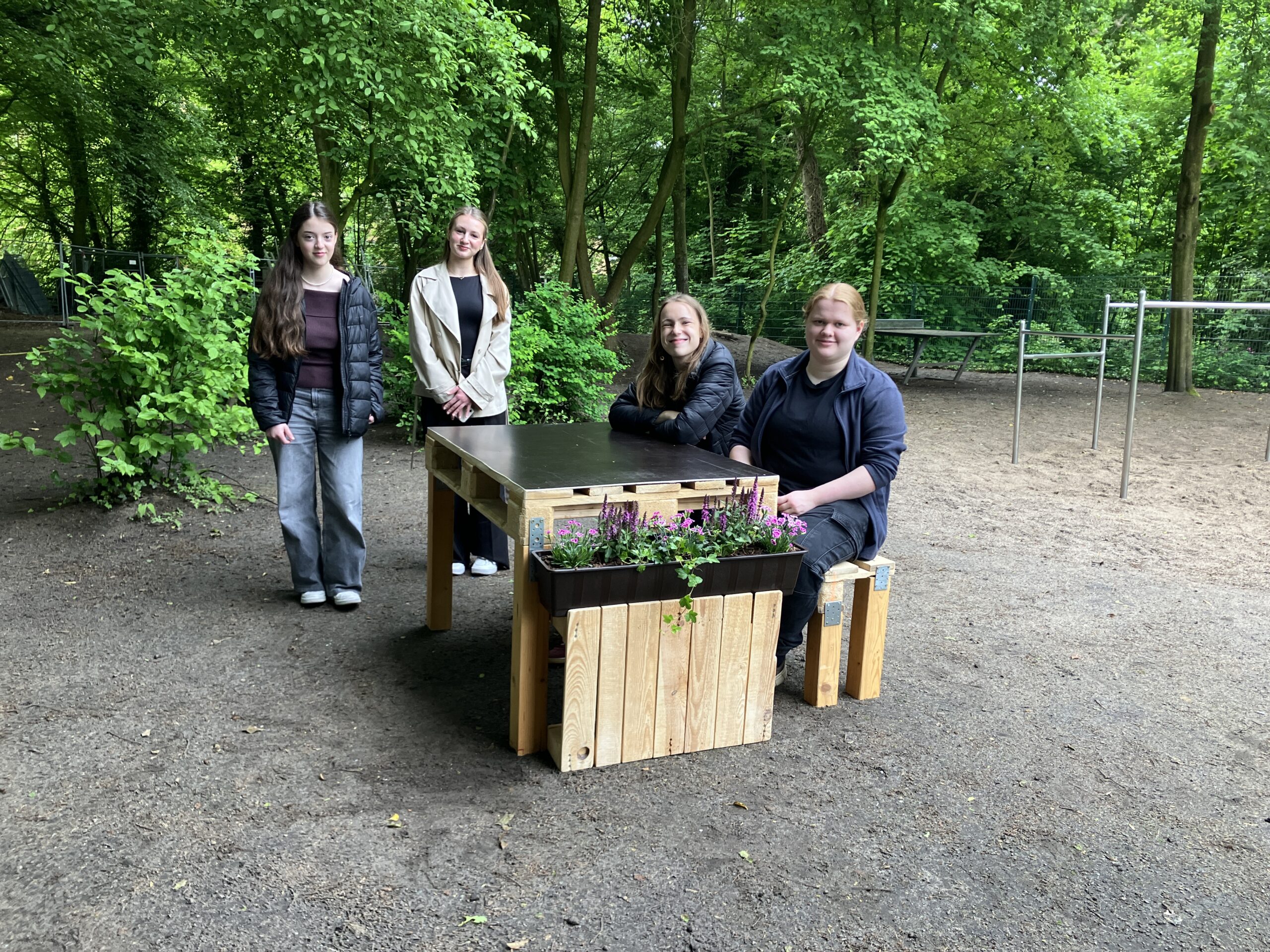 Eine Gruppe von Mädchen sitzt auf einer selbst gezimmerten Bank-Tisch-Kombination, an den Enden befinden sich Beetelemente