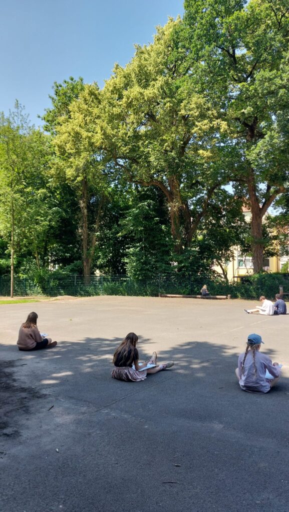 Mehrere Schülerinnen und Schüler sitzen auf dem Dobbenhof und zeichnen.