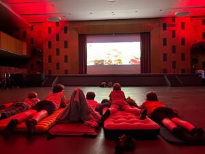 Schüler liegen in der Aula auf Matratzen und schauen auf die Leinwand.