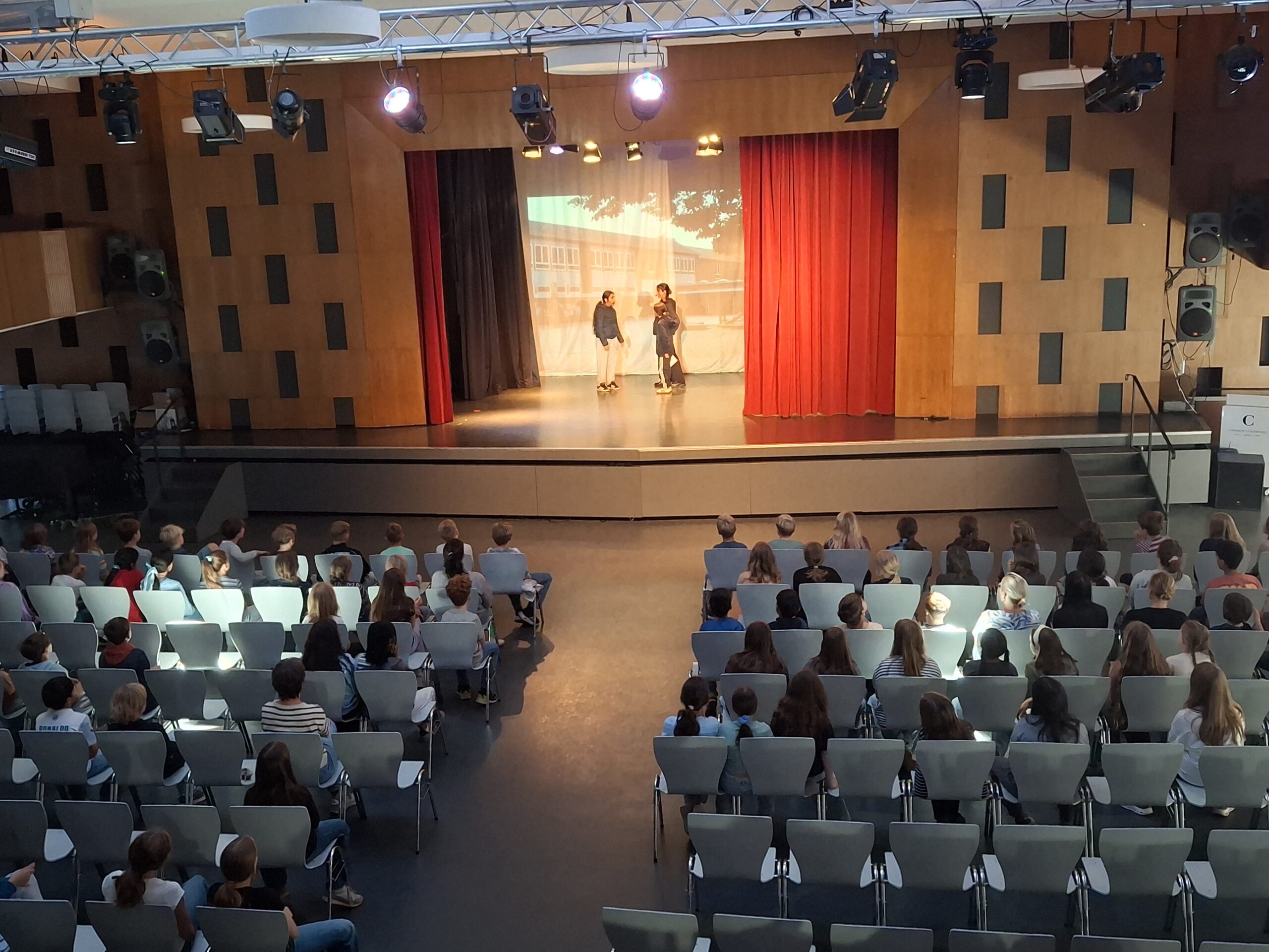 Theateraufführung in der Aula, auf der Bühne performen drei Schülerinnen