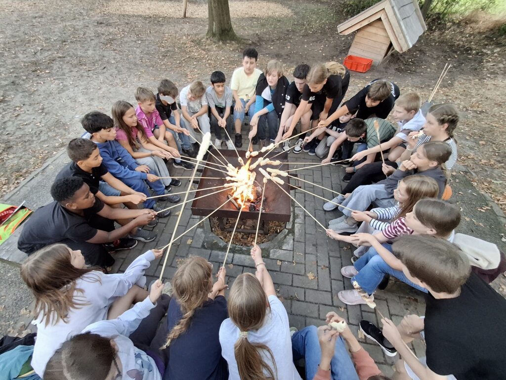 Schulklasse rund um ein Lagerfeuer backt Stockbrot